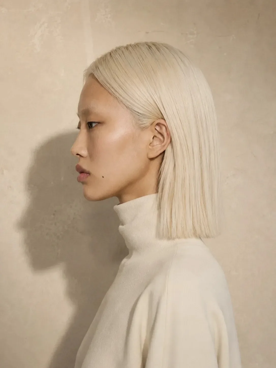 Synthetic model Aiko Velora in profile with straight platinum hair in an ivory cream turtleneck sweater