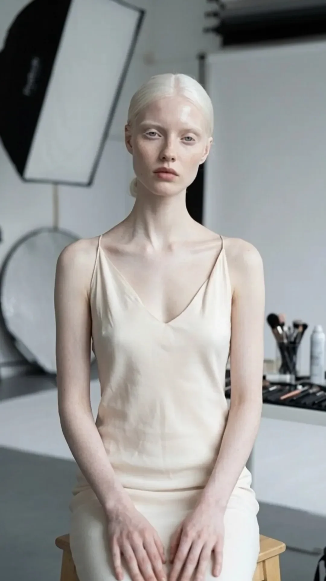 Synthetic model Milena Lindqvist seated in a photography lighting studio in a cream slip dress