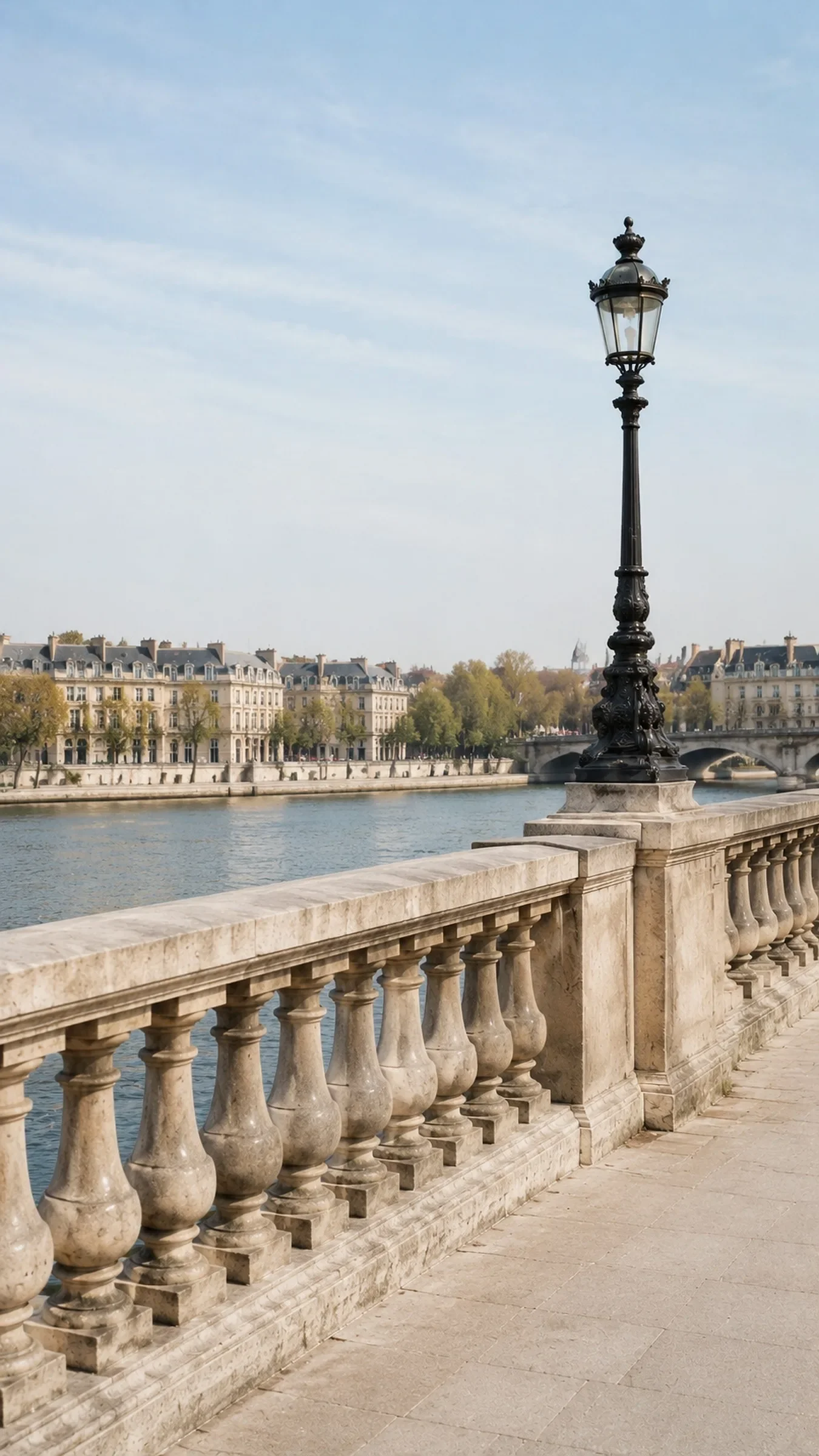 A stone balustrade and an iron lamp post on a Paris quay beside the river on a clear spring day
