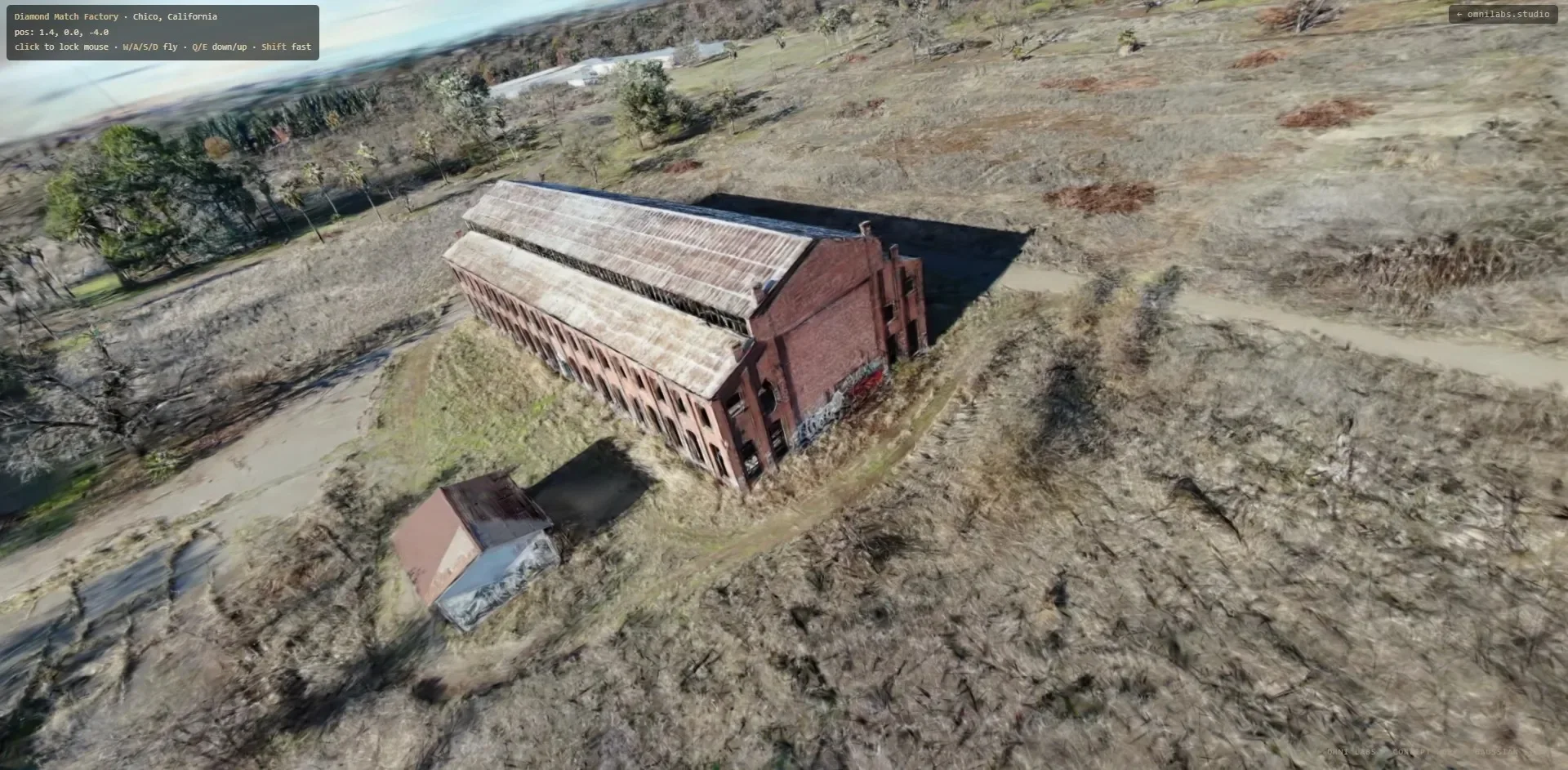 Three-quarter aerial view of a 3D Gaussian splat reconstruction of an industrial brick factory facade and terrain